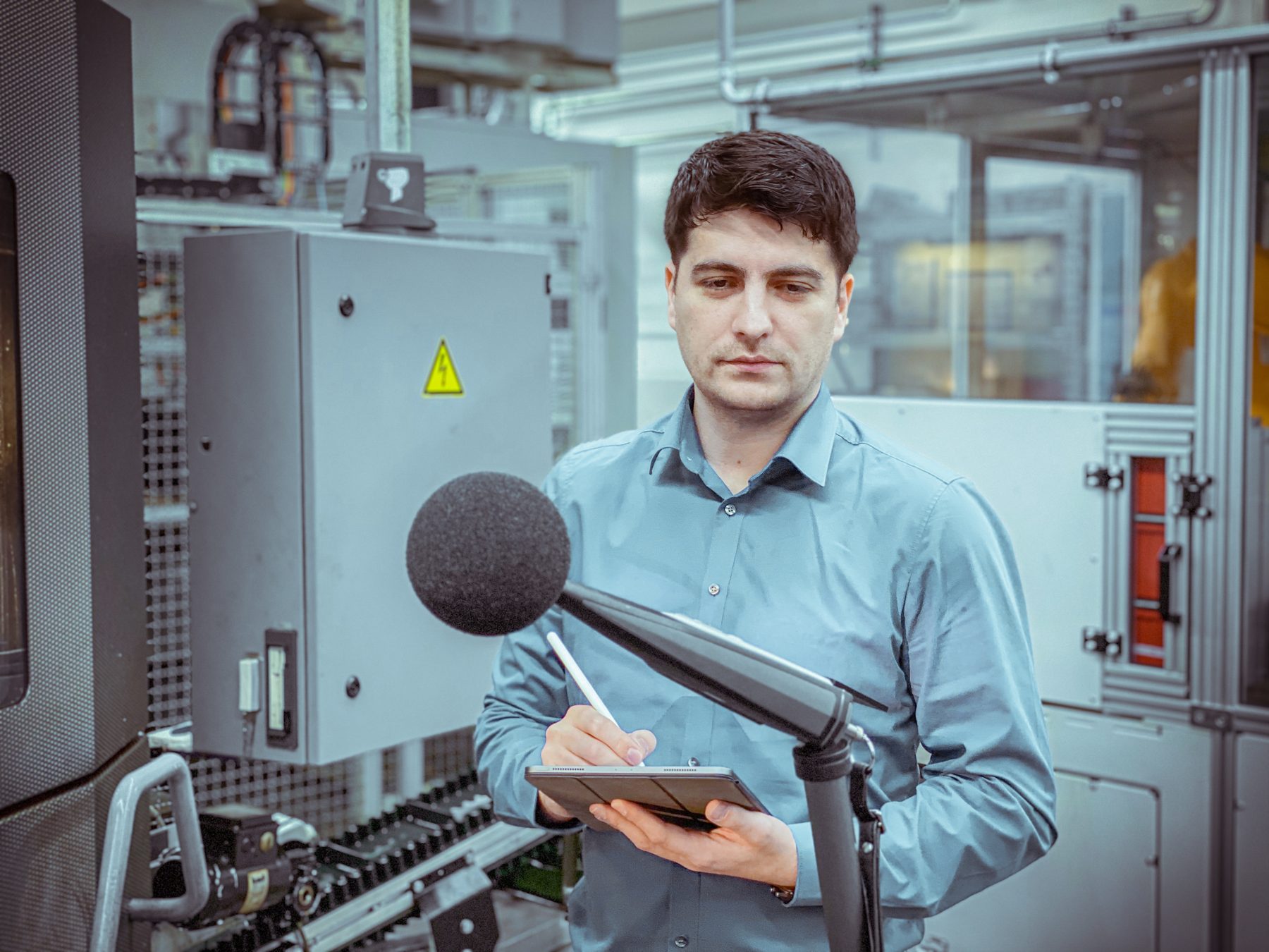 Orhan Cicekli bei einer Messung in einer Produktionshalle, mit Schallpegelmesser und Tablet