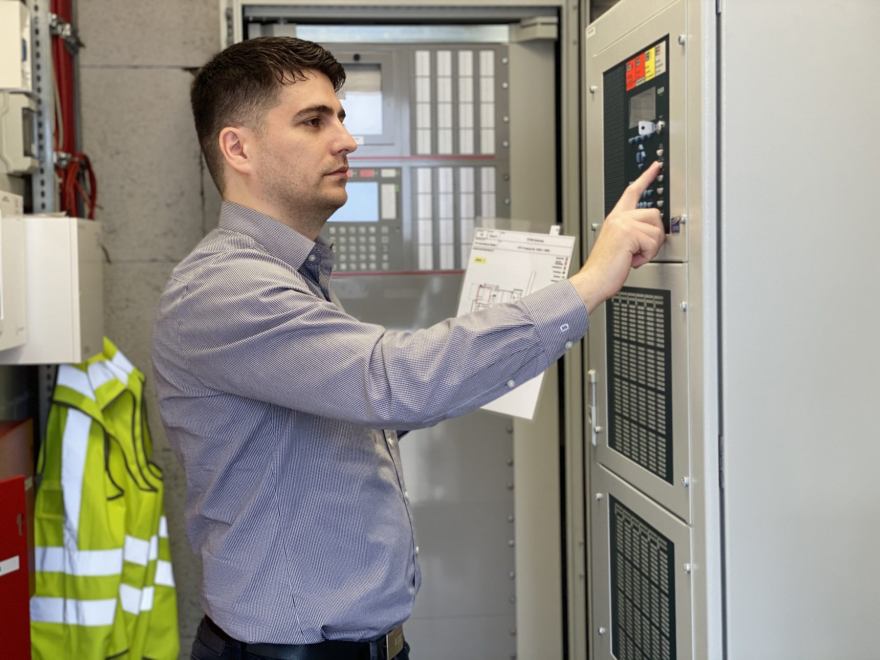 Orhan Cicekli prüft eine Brandmeldezentrale, den Feuerwehrplan in der Hand